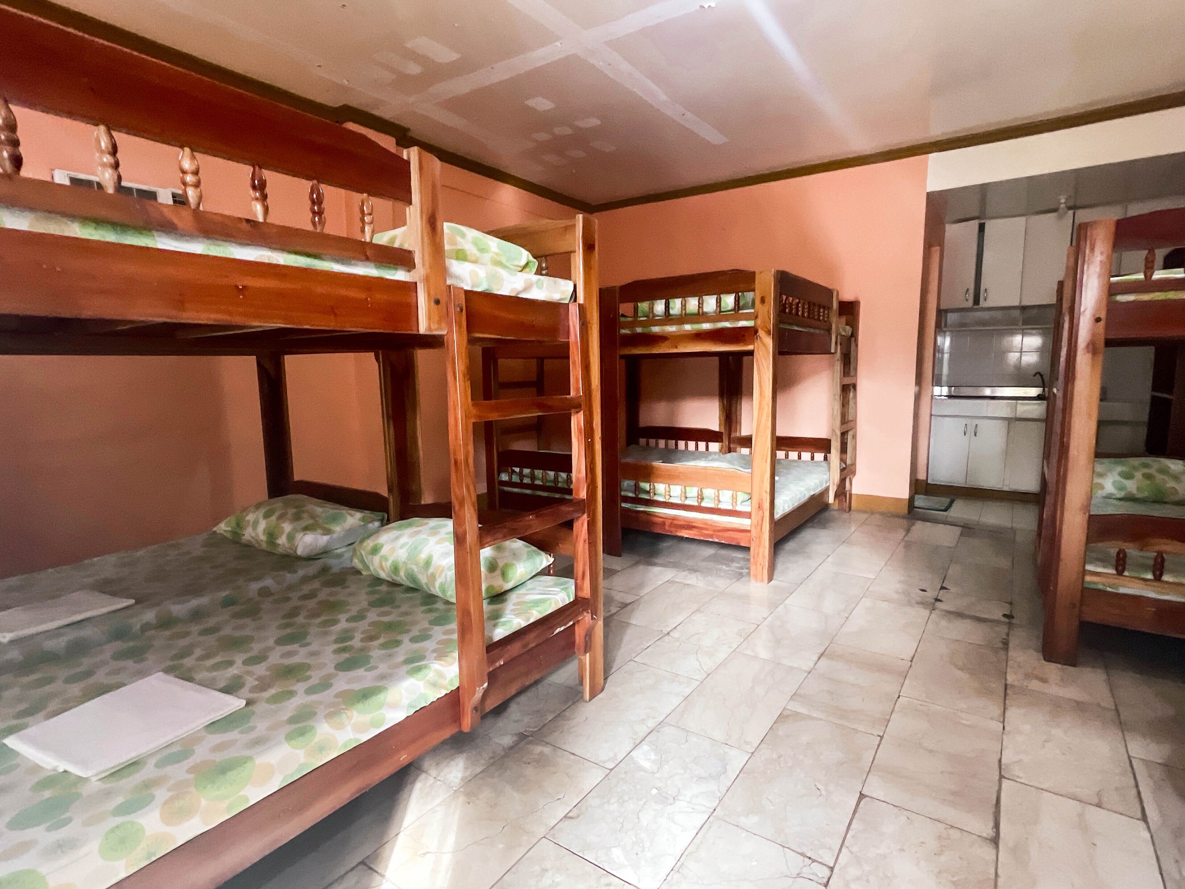 A dormitory room with bunk beds, a kitchenette, and a tiled floor.
