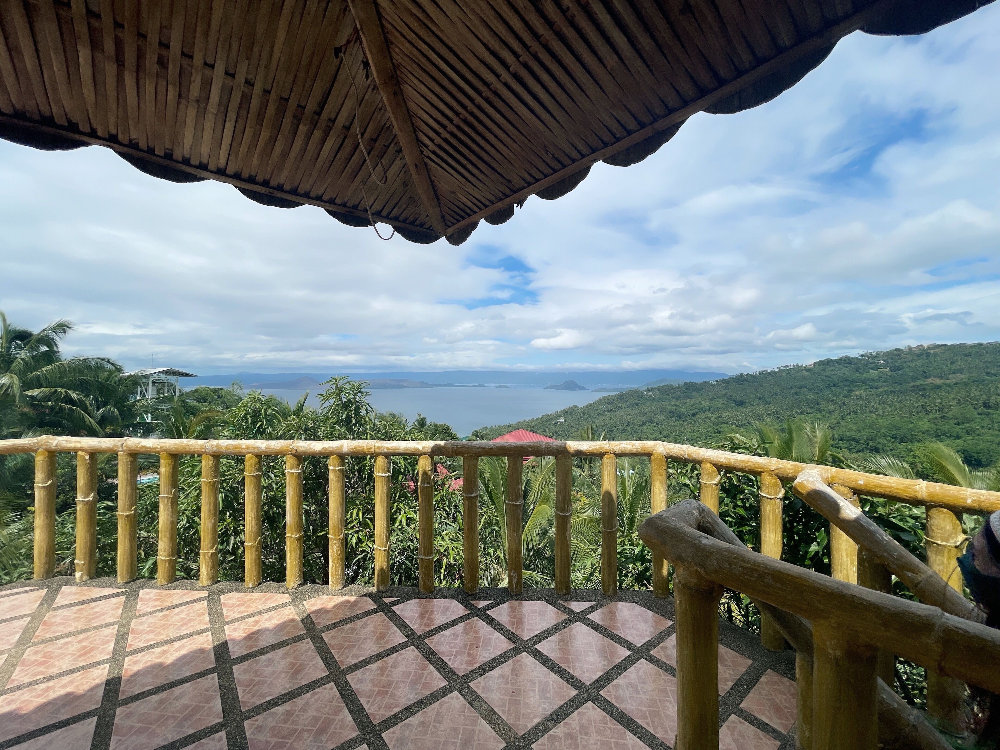 A wooden balcony with a tiled floor, overlooking a scenic view of a body of water and lush greenery.