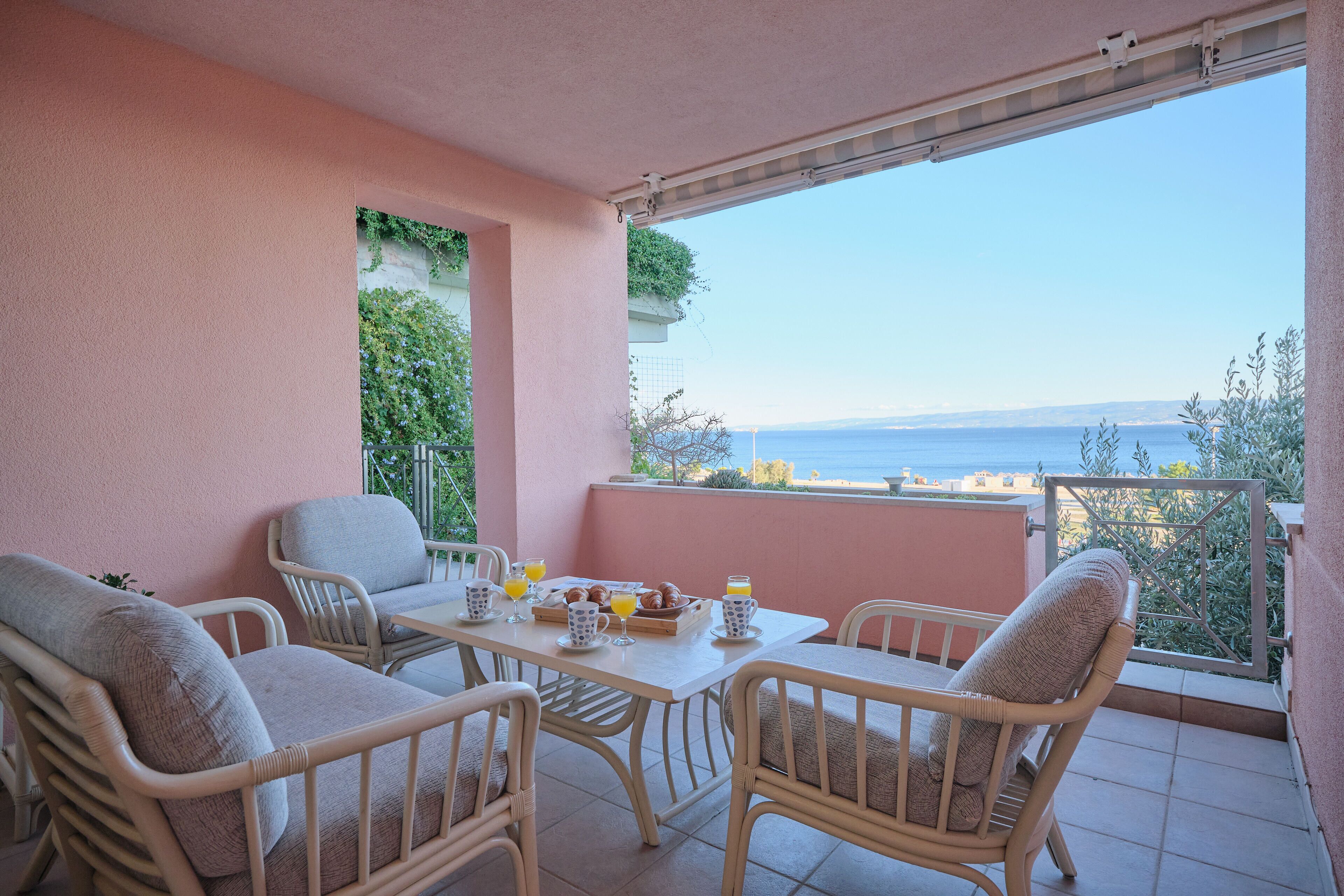 Een balkon met rieten meubilair, een tafel met ontbijtartikelen en uitzicht op zee.