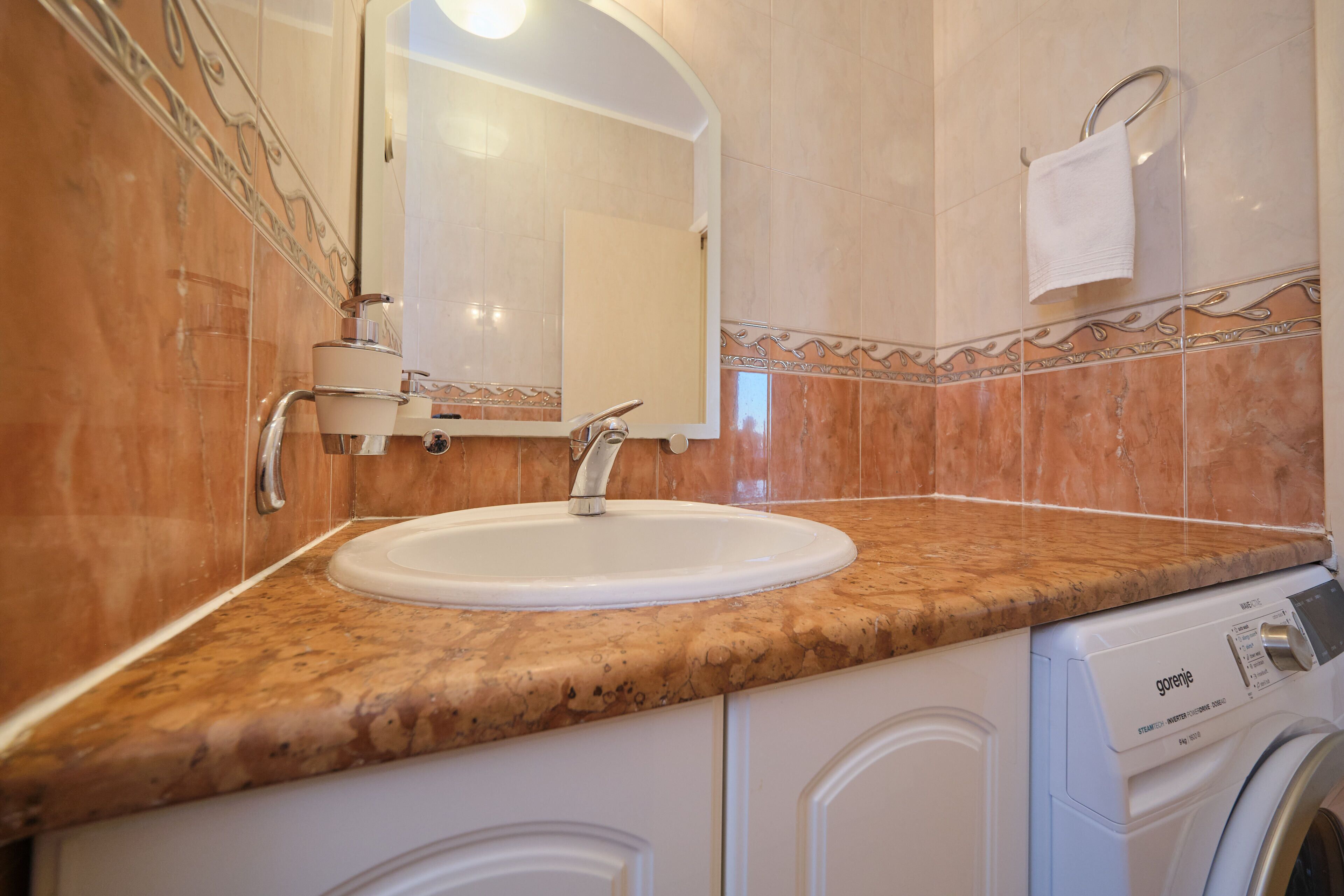 A bathroom with a sink, mirror, towel rack, and a washing machine.