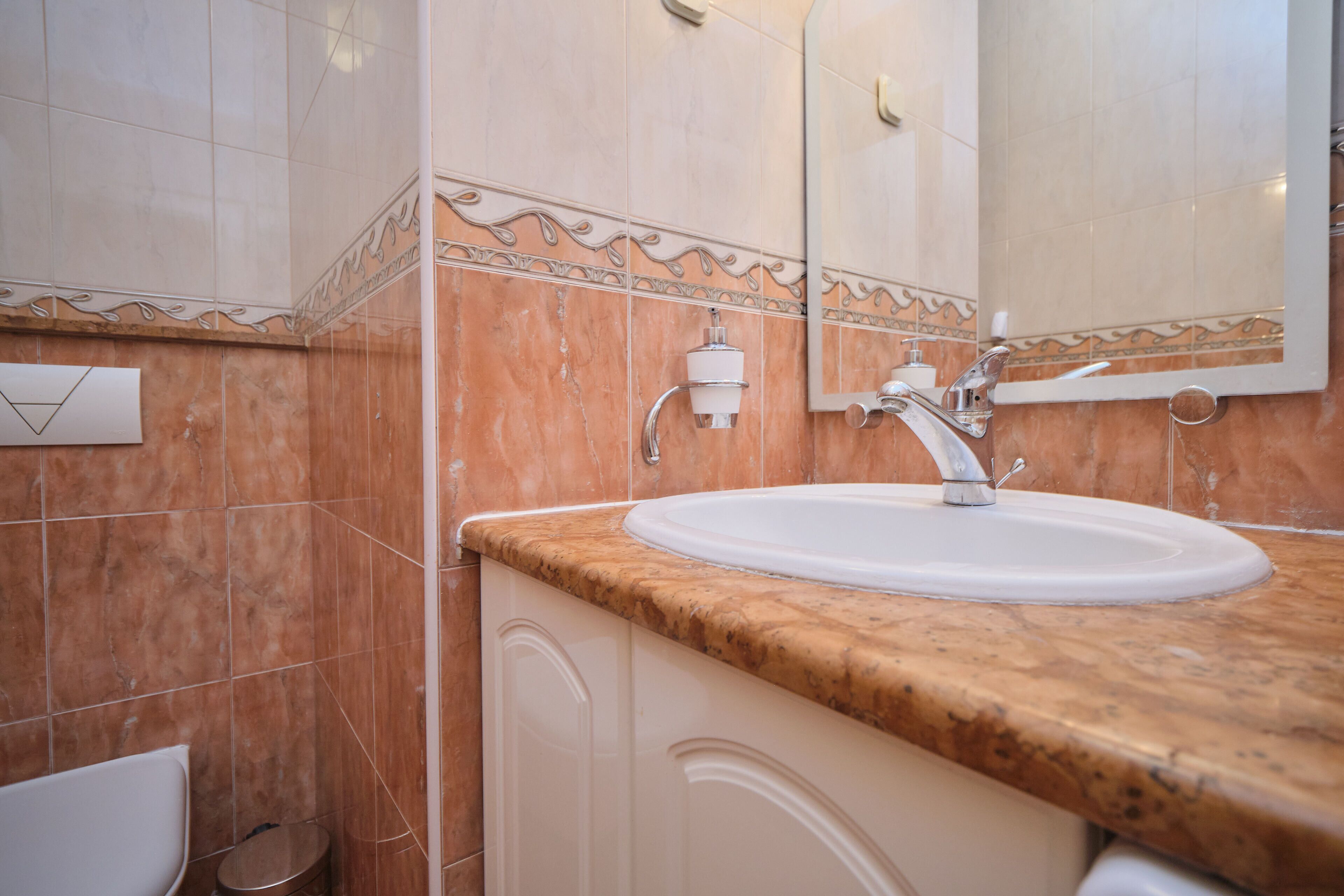 Un baño con un lavamanos blanco, un espejo y un perchero para toallas.