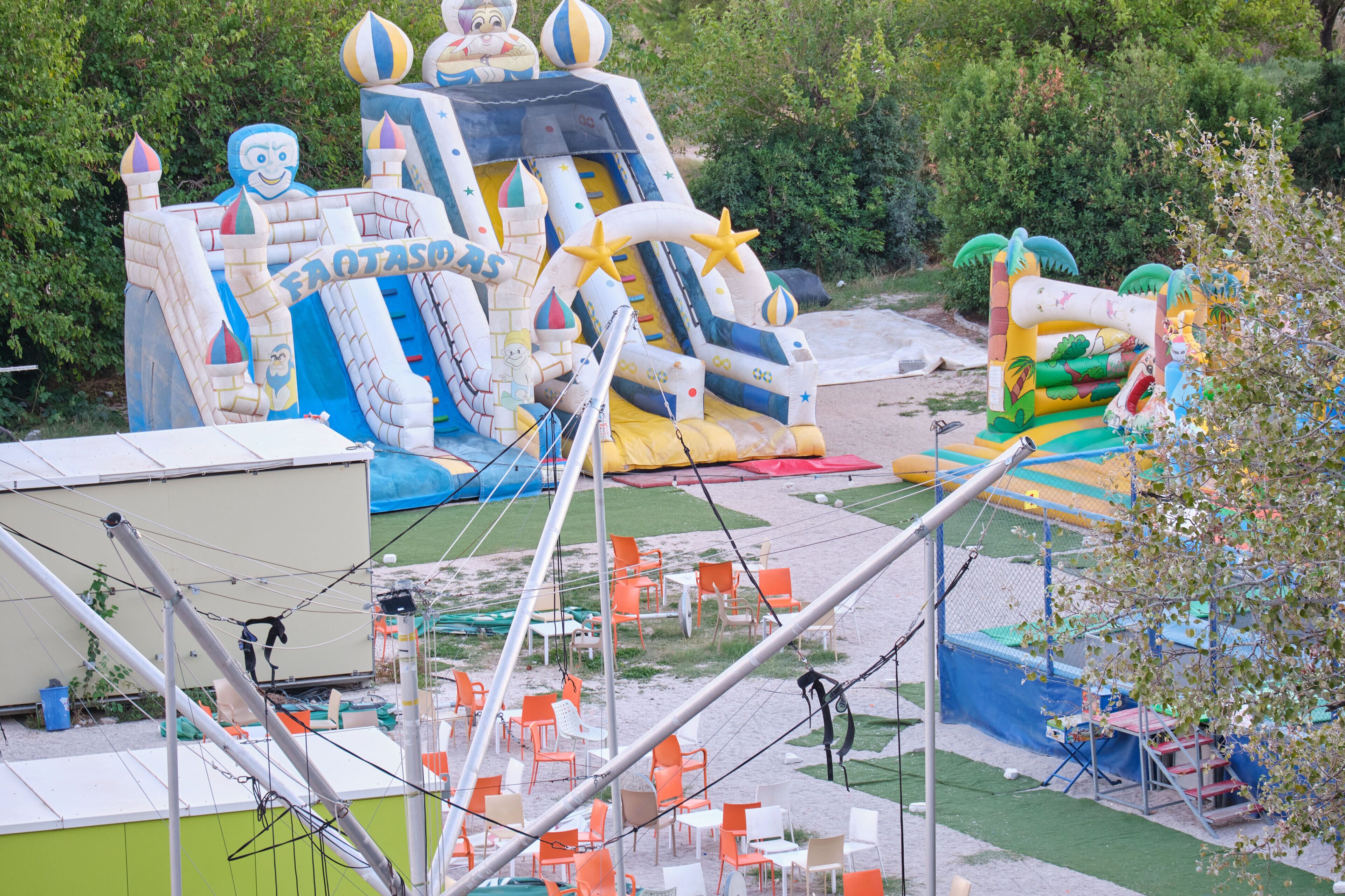 An inflatable play structure with slides and climbing areas, surrounded by outdoor seating and a fenced area.