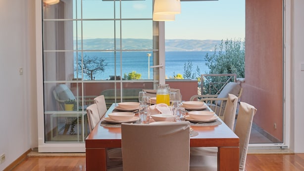 A dining area with a table set for four, a large window with a view of the sea, and a hanging pendant light. - Holiday Seaview Apartment by Litto (Split)