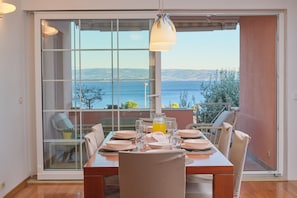 A dining area with a table set for four, a large window with a view of the sea, and a hanging pendant light.