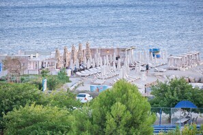Relax on the beachside promenade with sun loungers and umbrellas, surrounded by trees and shrubs.