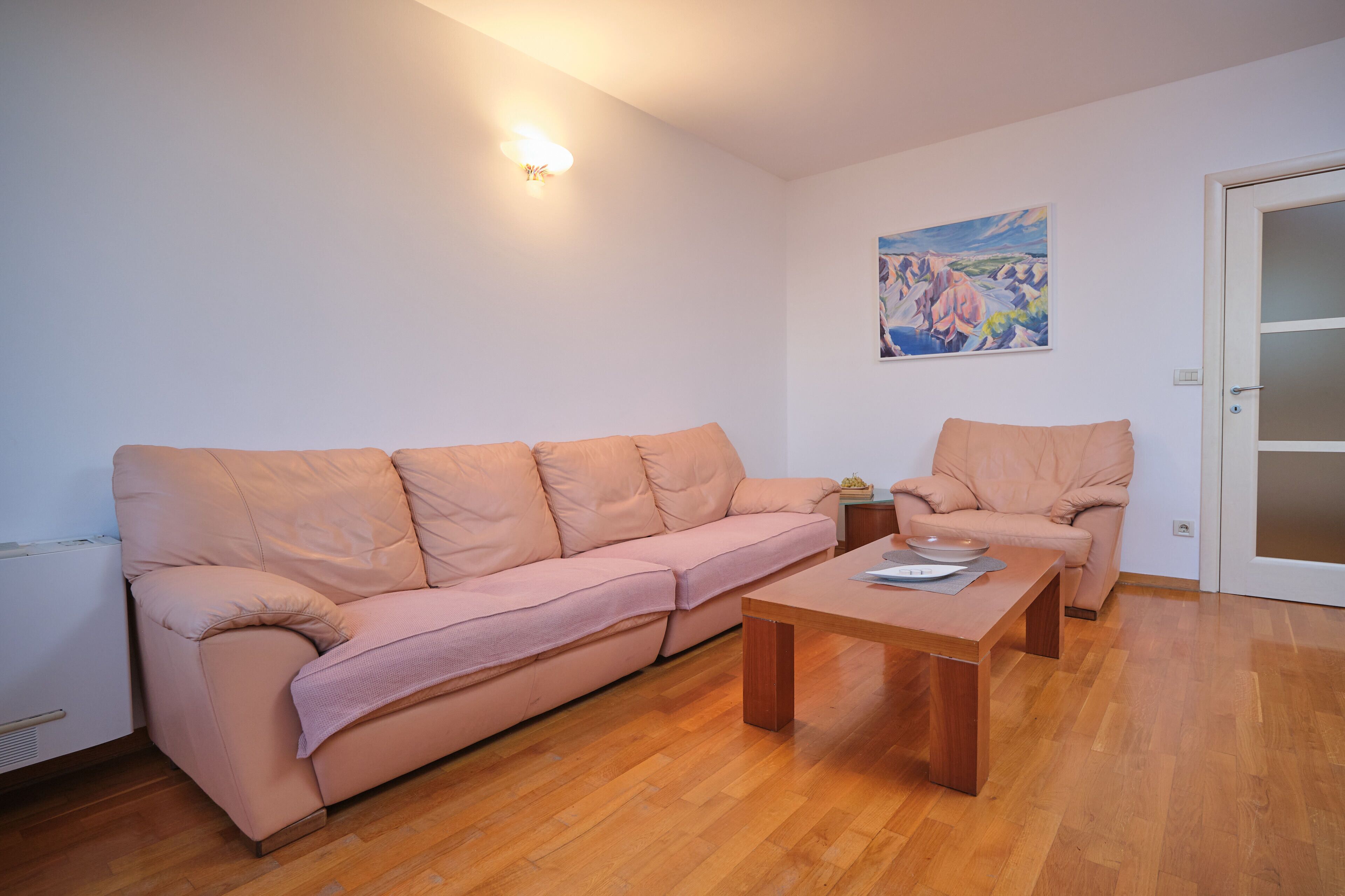 Un salon avec un canapé, un fauteuil, une table basse en bois et un tableau accroché au mur.