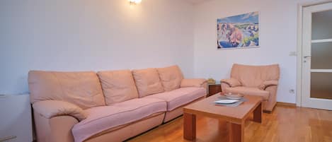 Una sala de estar con un sofá, un sillón, una mesa de centro de madera y un cuadro en la pared.