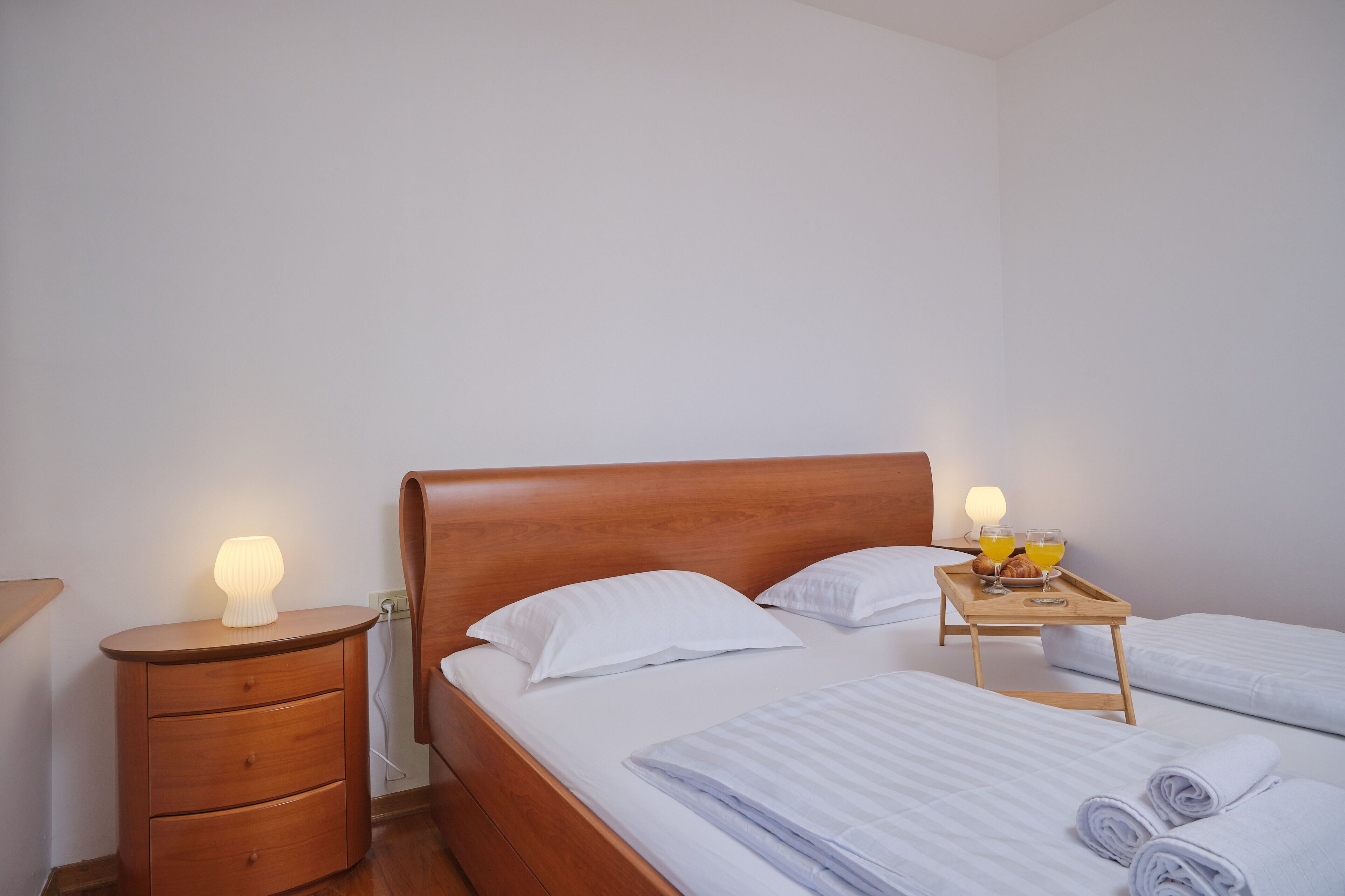 A neatly made bed with white linens, a wooden bedside table with a lamp, and a tray with breakfast items.