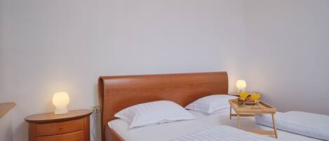 A neatly made bed with white linens, a wooden bedside table with a lamp, and a tray with breakfast items.