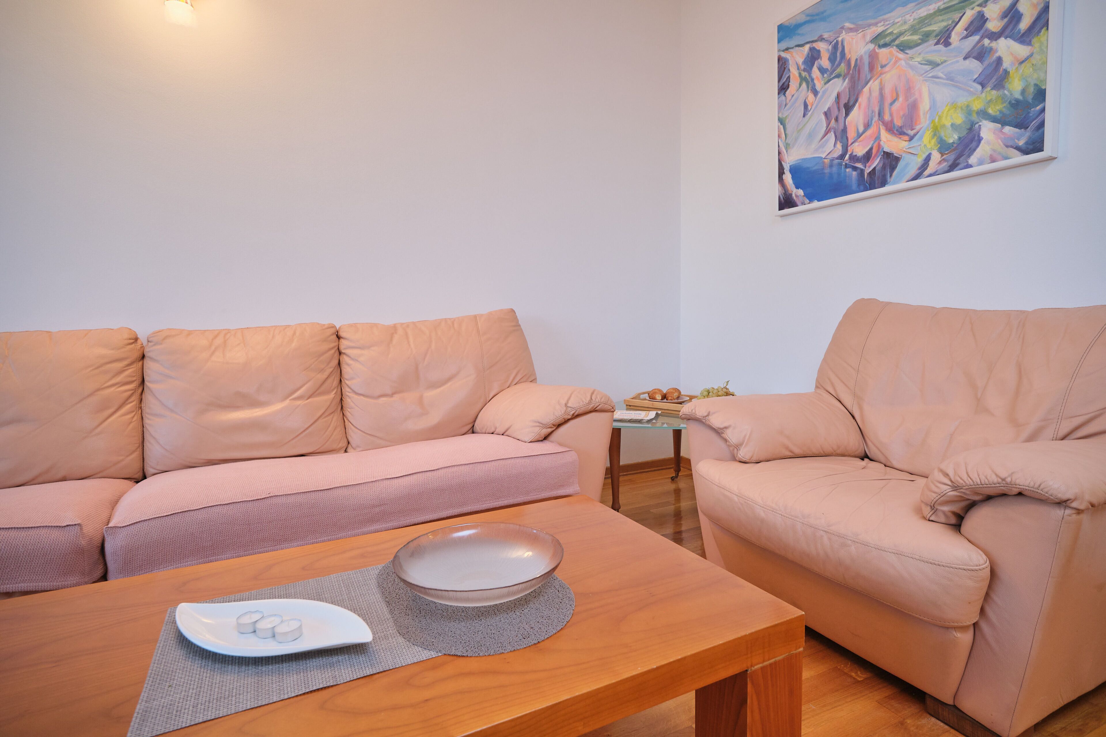 A living room with a beige sofa, a wooden coffee table with a bowl and a placemat, and a painting on the wall.