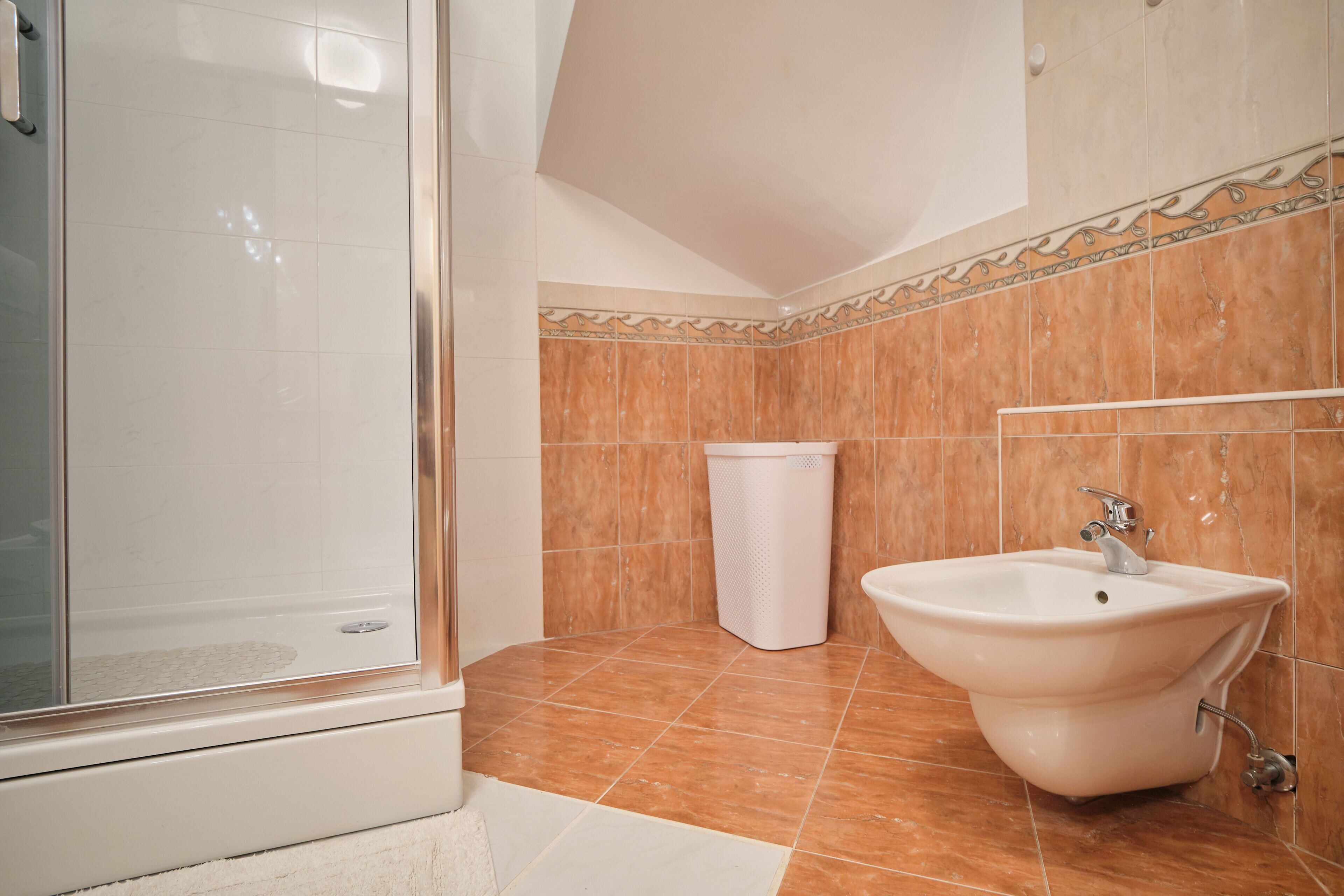 A bathroom with a shower, a sink, and a trash bin.