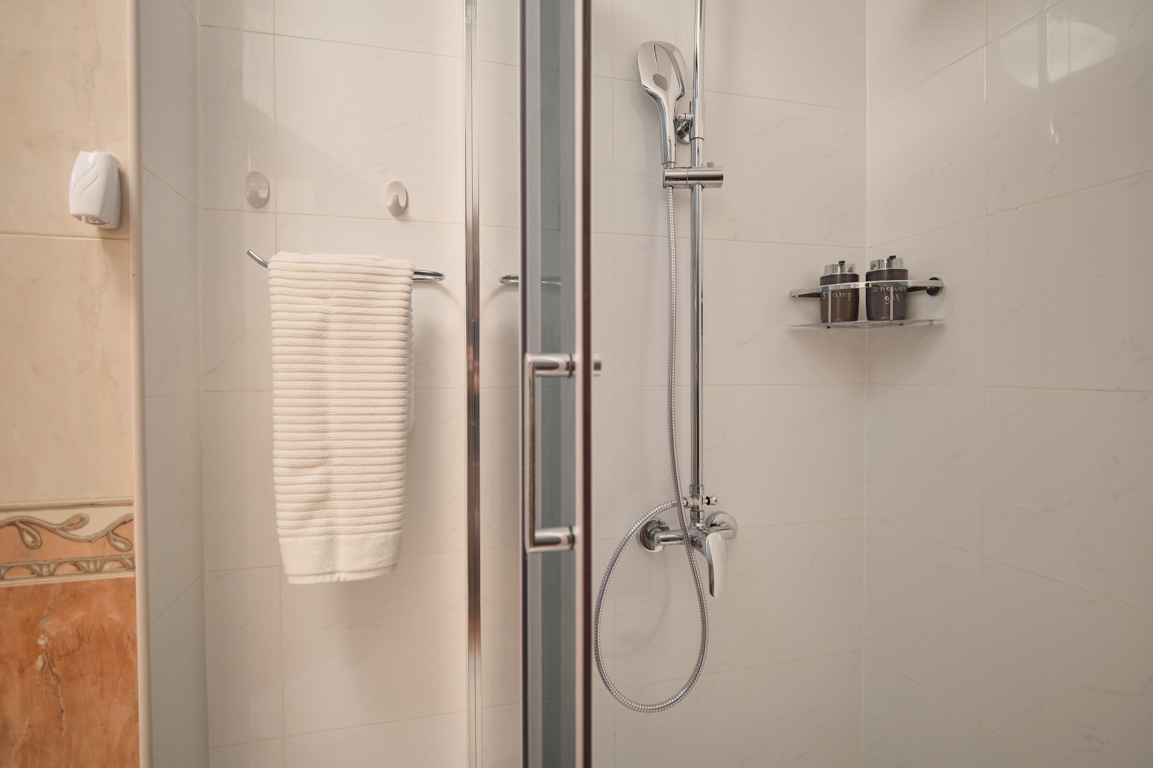 Et moderne badeværelse med en brusekabine i glas, et håndklædestativ og en hylde med toiletartikler.