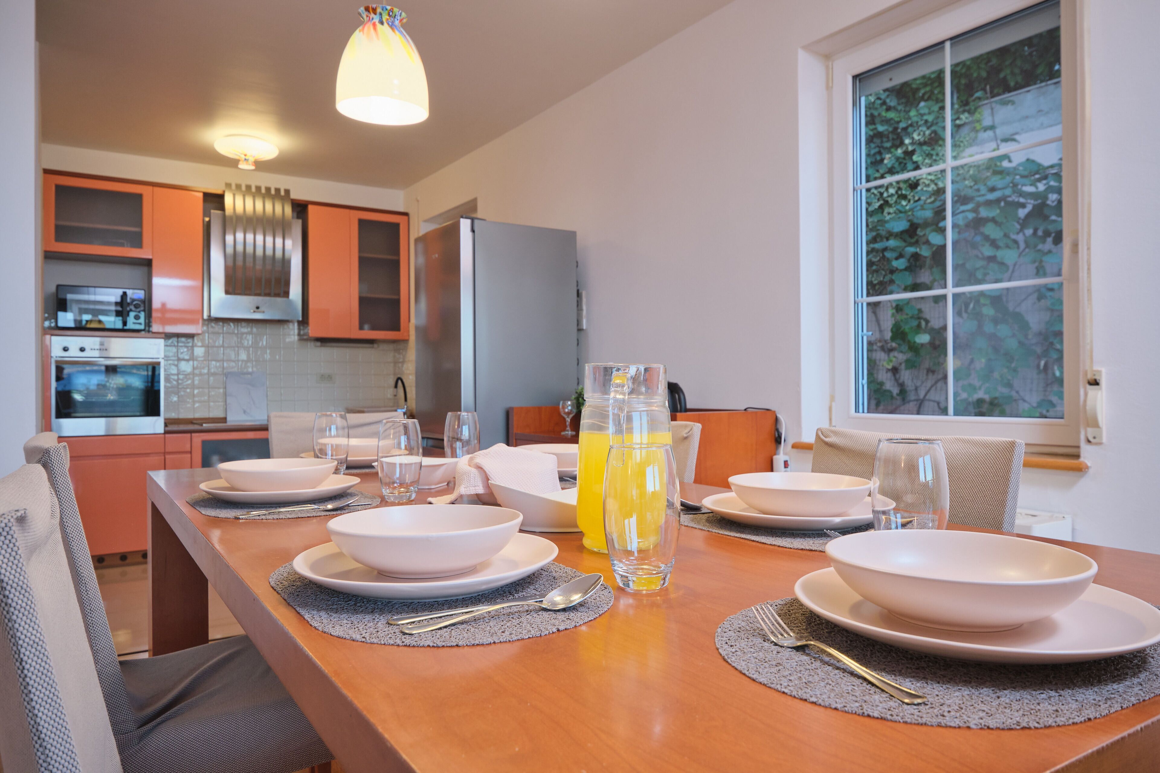 A dining table set with white plates, bowls, and cutlery, with a bottle of orange juice and glasses.