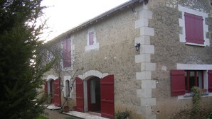 Un bâtiment aux portes et fenêtres rouges, aux murs en pierre et à l’allée gravillonnée.