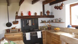 Une cuisine équipée d’une cuisinière, de meubles en bois, d’ustensiles suspendus et d’une fenêtre donnant sur un beau paysage.