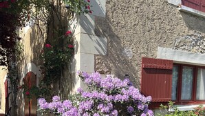 Un mur de pierre avec une porte en bois et une fenêtre aux volets rouges.