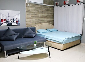 Een slaapkamer met een bed, een bank, een glazen salontafel en een wandairconditioner.