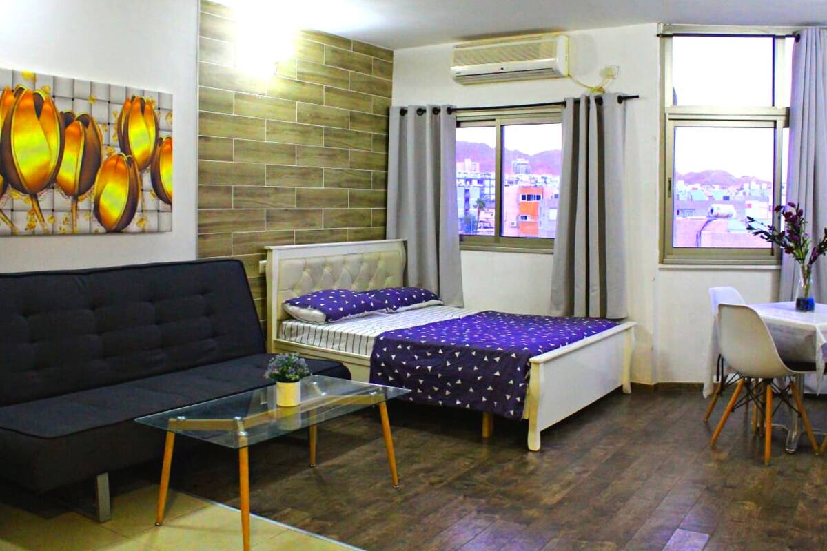 A compact hotel room with a bed, a sofa, a small table, and a window with a view.