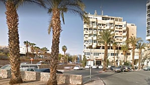 A multi-story building with balconies and air conditioning units, surrounded by palm trees and parked cars. - Eilat Apartments  (Eilat)