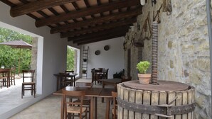 Une terrasse extérieure avec des tables et des chaises en bois, des murs en pierre et une cheminée rustique.