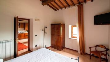 Un dormitorio con cama, armario de madera, televisor y ventana con cortinas.