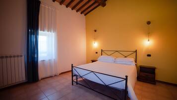 Une chambre à coucher avec un lit, une table de chevet, une lampe fixée au mur et une fenêtre avec des rideaux.