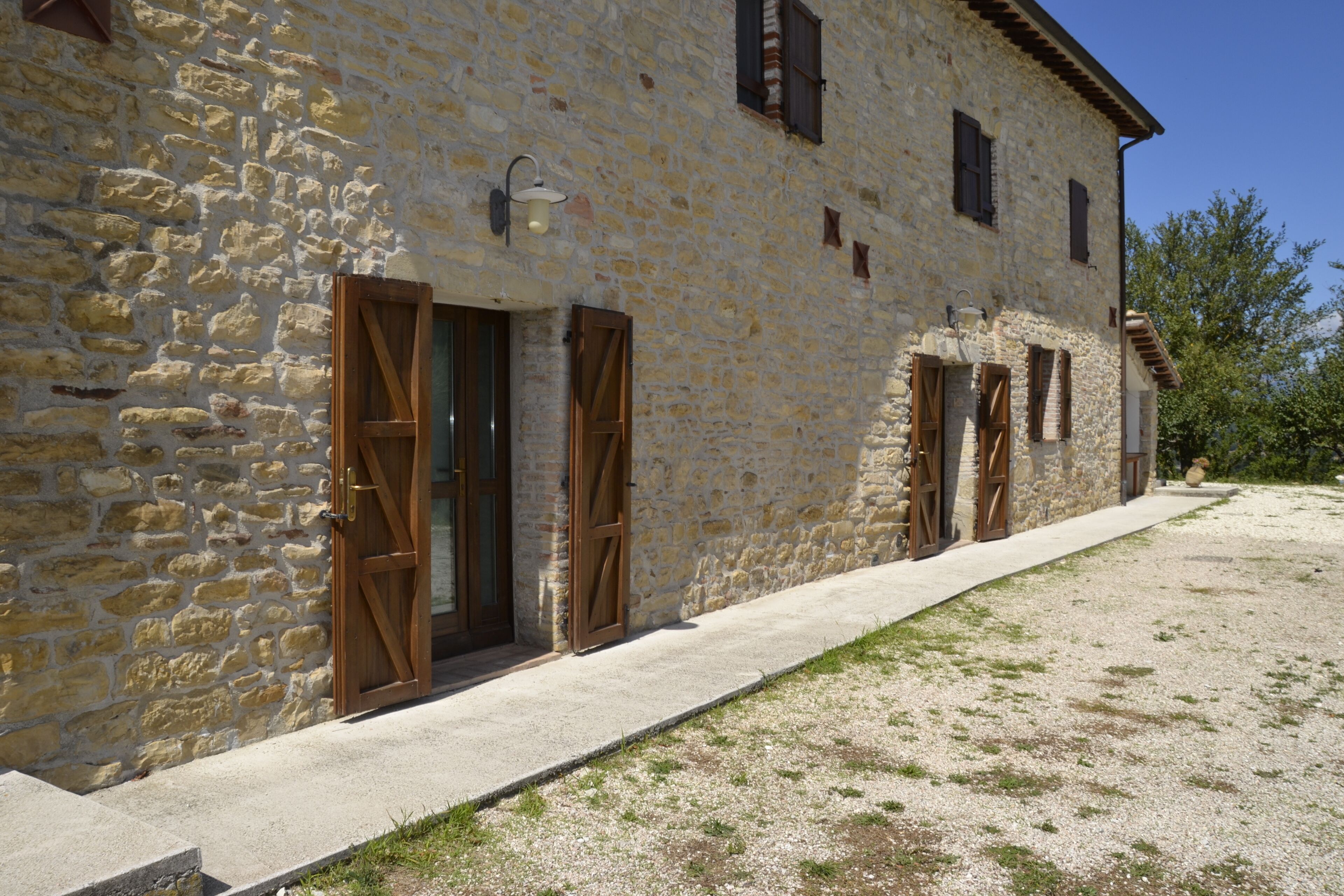 A stone building with wooden shutters and a concrete pathway.