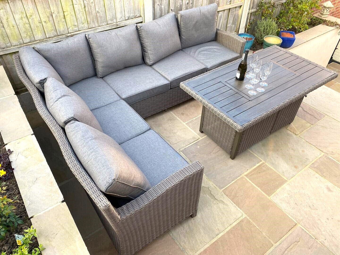 A sectional sofa with cushions, a matching ottoman, and a wooden coffee table with a bottle and glasses on it.