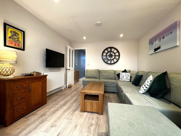 A living room with a sofa, a coffee table, a TV, a wall clock, and a cabinet.