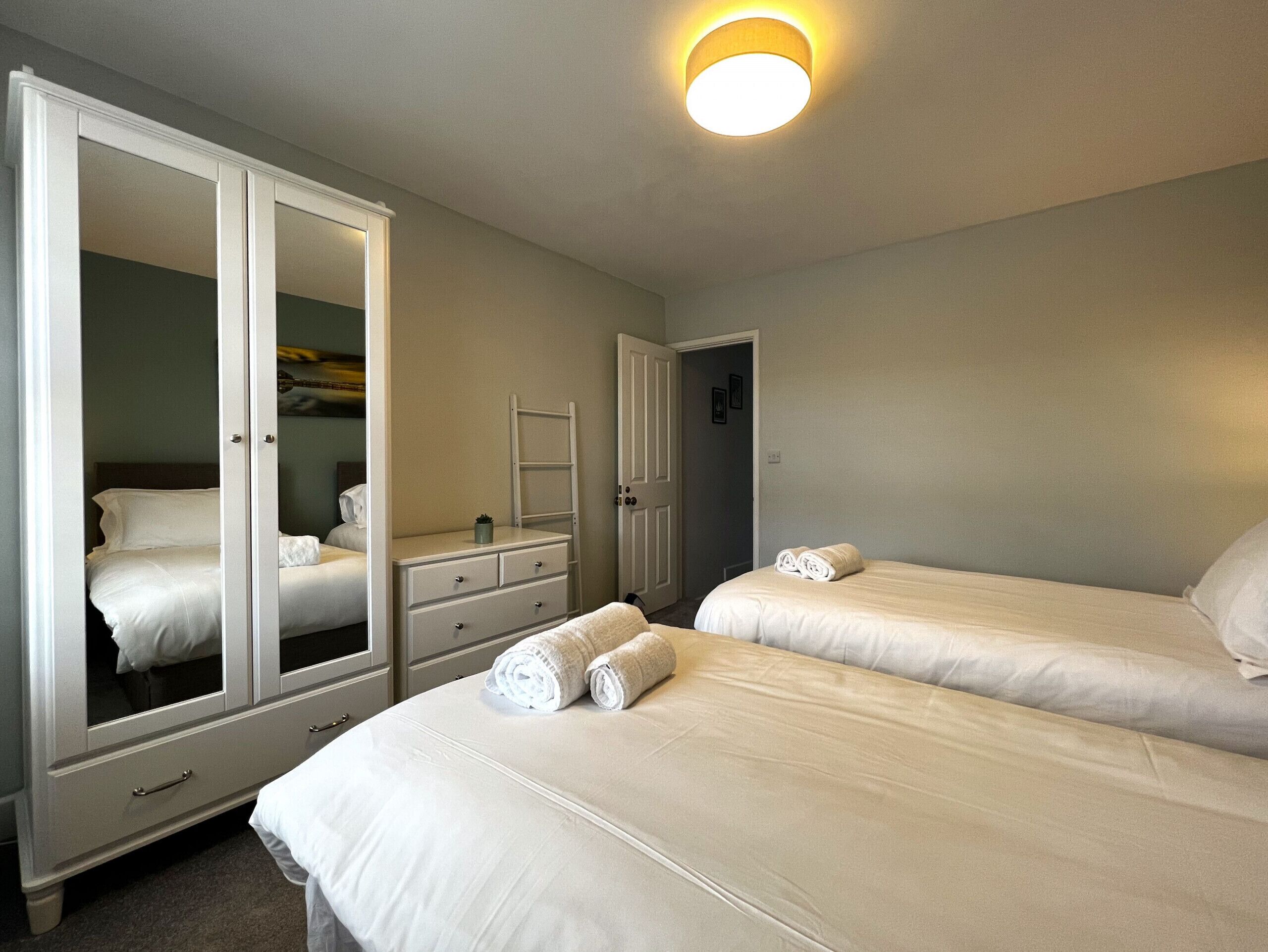 A bedroom with two beds, a wardrobe, a dresser, and a mirror.