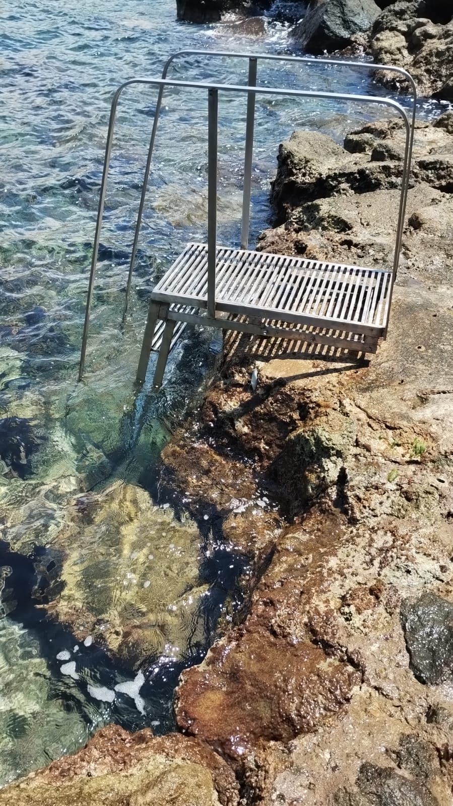 A metal chair partially submerged in clear water, with rocky terrain in the background.