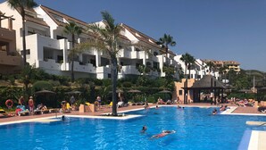Una piscina con persone che nuotano e si rilassano al sole, circondata da palme e lettini.