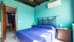 A bedroom with a bed, a nightstand, a dresser, and an air conditioning unit on the wall.