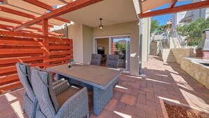 An outdoor patio with a table and chairs, a wooden pergola, and a stone wall. - Anovi Holiday House by Litto (Okrug)