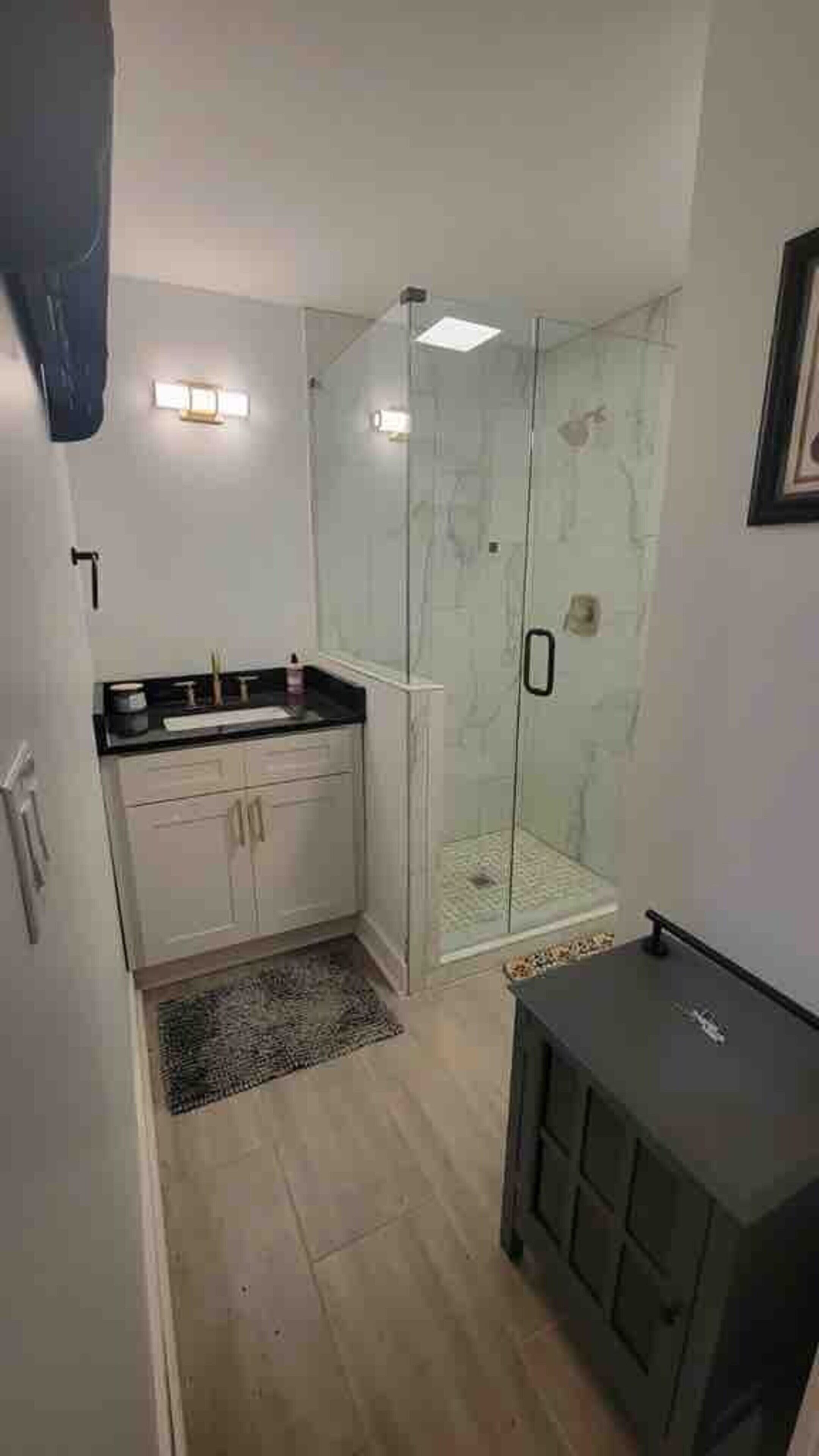 Un baño con cabina de ducha de vidrio, un lavabo con encimera y un mueble pequeño.