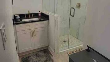 A bathroom with a glass shower enclosure, a sink with a countertop, and a small cabinet.