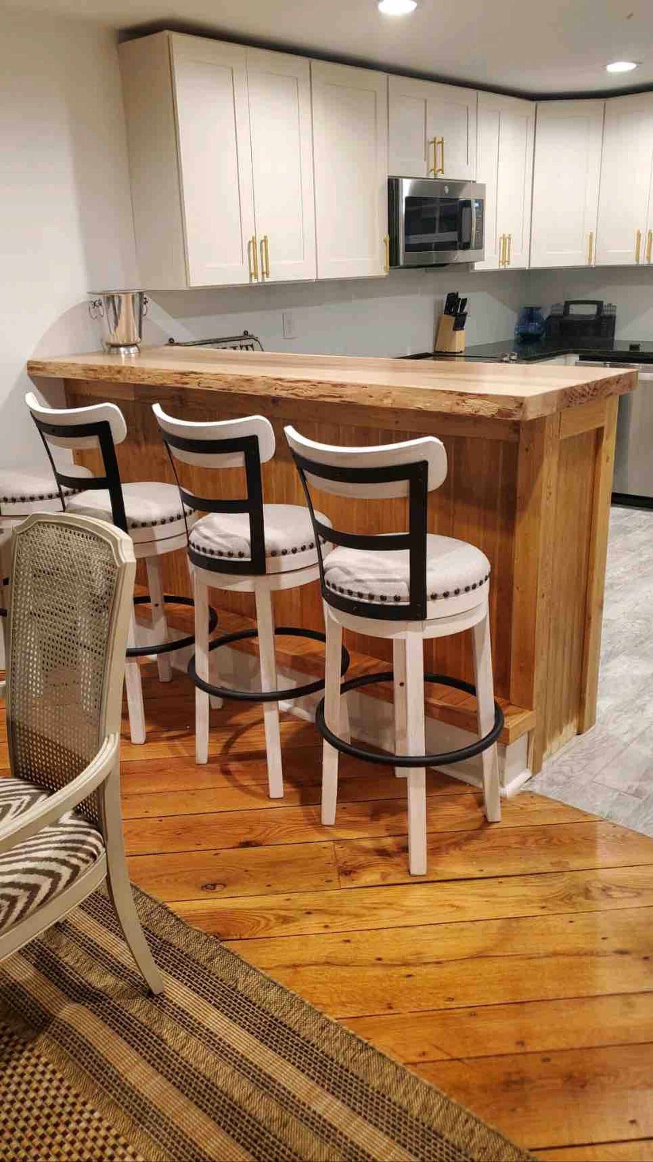 A kitchen with white cabinets, a stainless steel refrigerator, and a wooden island with bar stools.