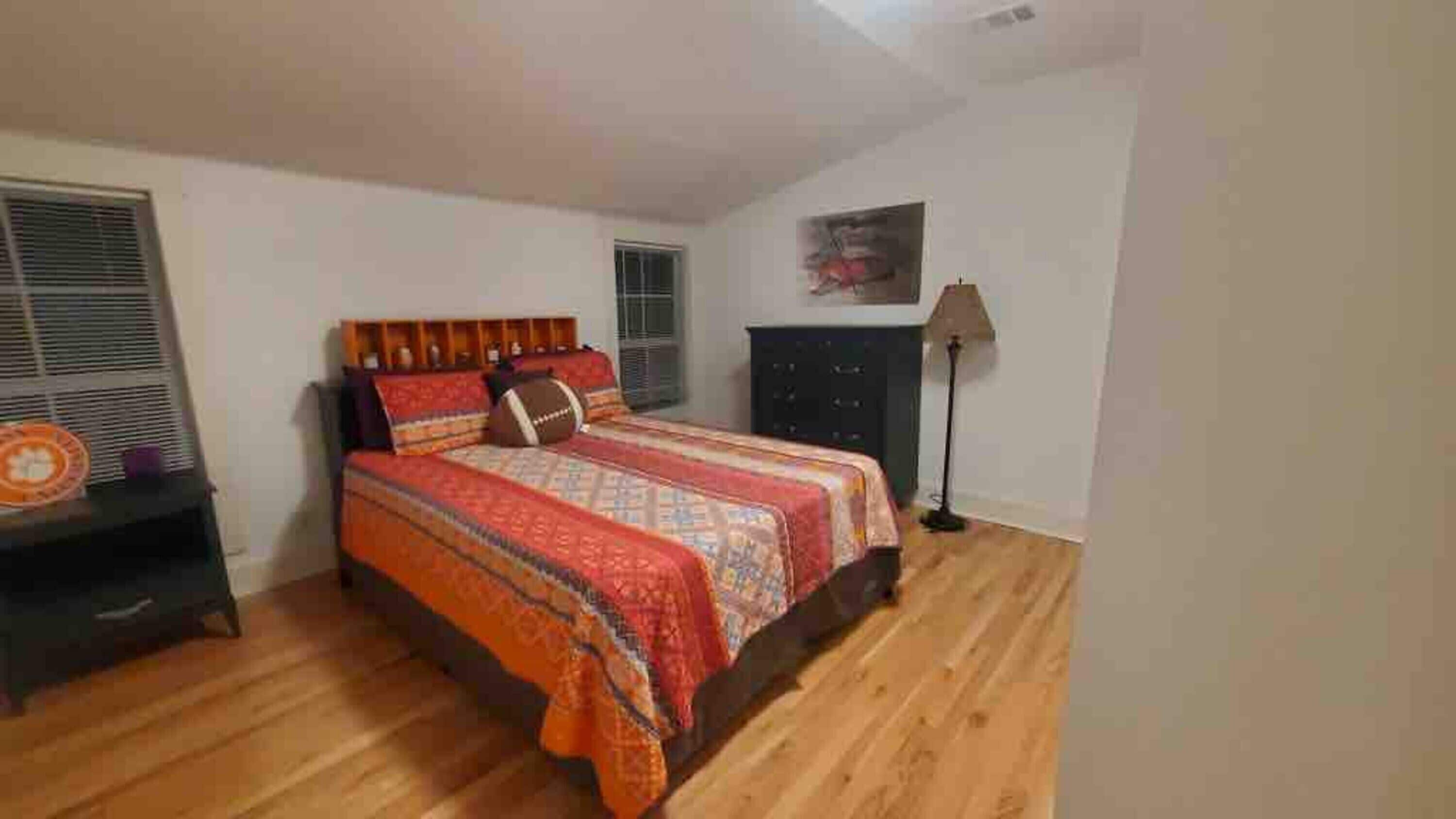 A bedroom with a bed, a dresser, a lamp, and a window.