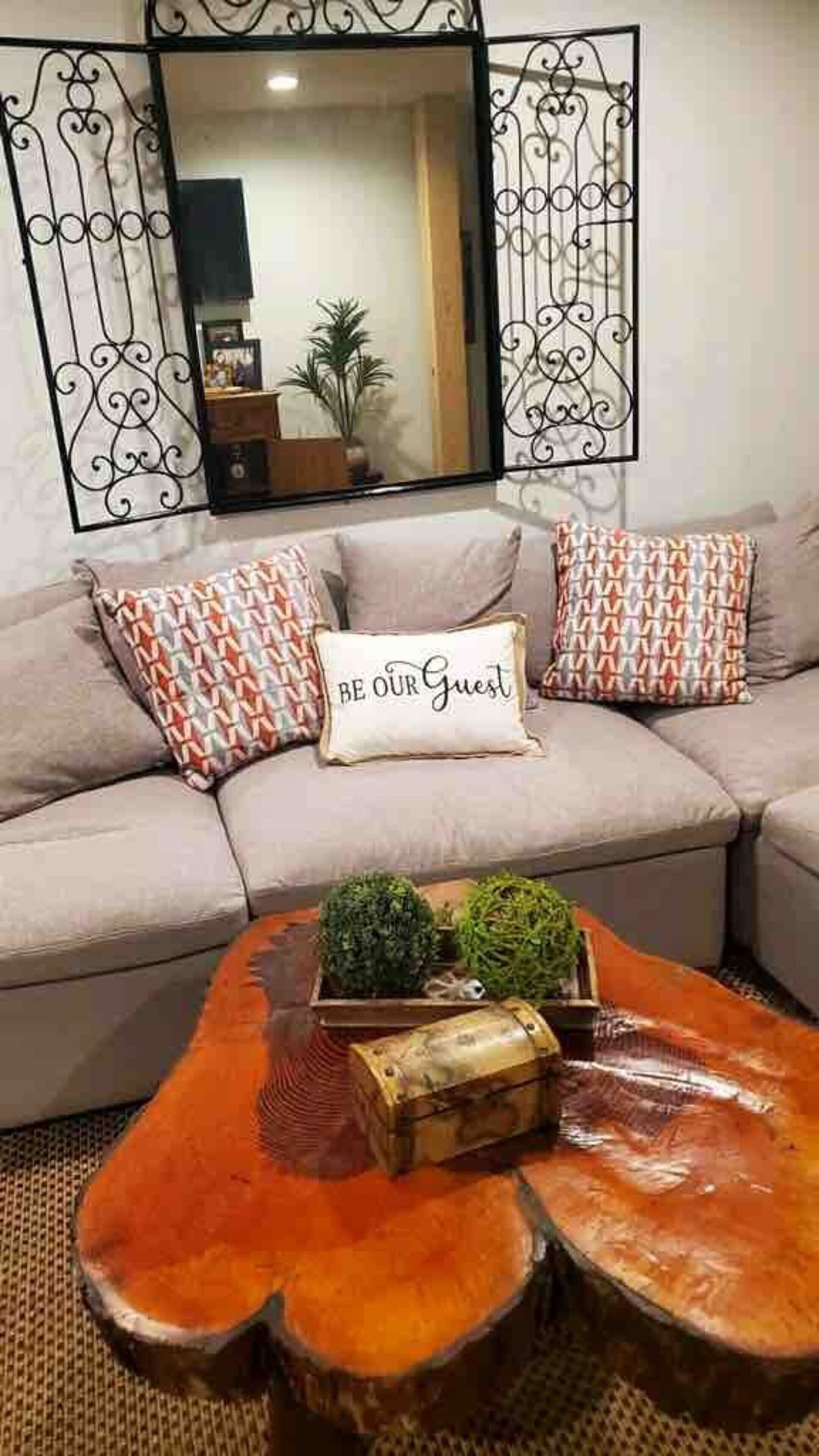 A living room with a sofa, decorative pillows, a mirror, and a coffee table with a plant and a small chest.
