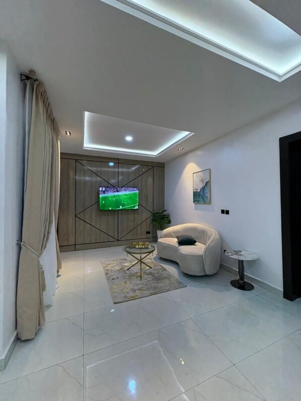 A modern living room with a flat-screen TV, a sofa, a coffee table, and a small side table. - DELIZ HOMES AND HOTEL (Lekki)