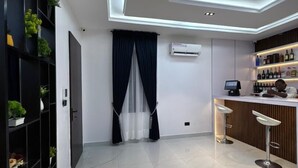 A modern bar area with a white countertop, two bar stools, and a shelf with bottles. - DELIZ HOMES AND HOTEL (Lekki)