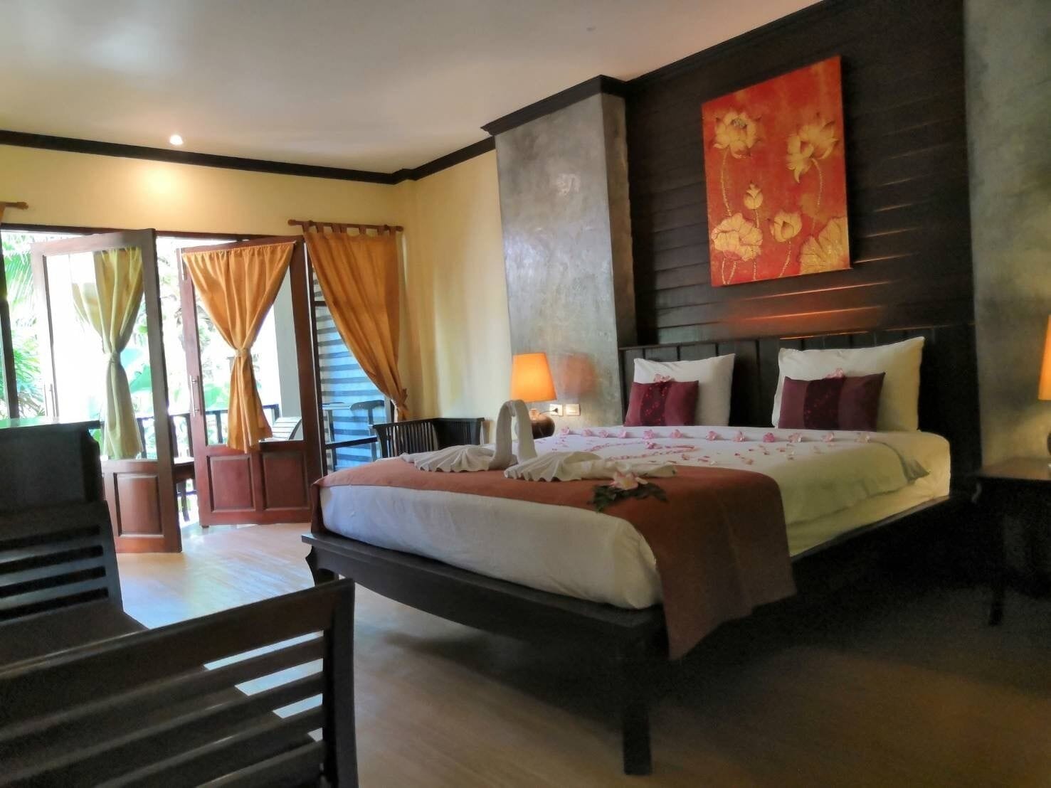 A hotel room with a large bed, a desk, a chair, and a view of the outdoors through a window with curtains.
