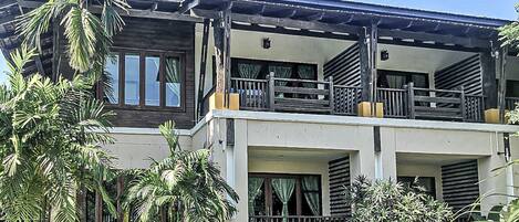 A two-story building with a balcony, surrounded by tropical vegetation.