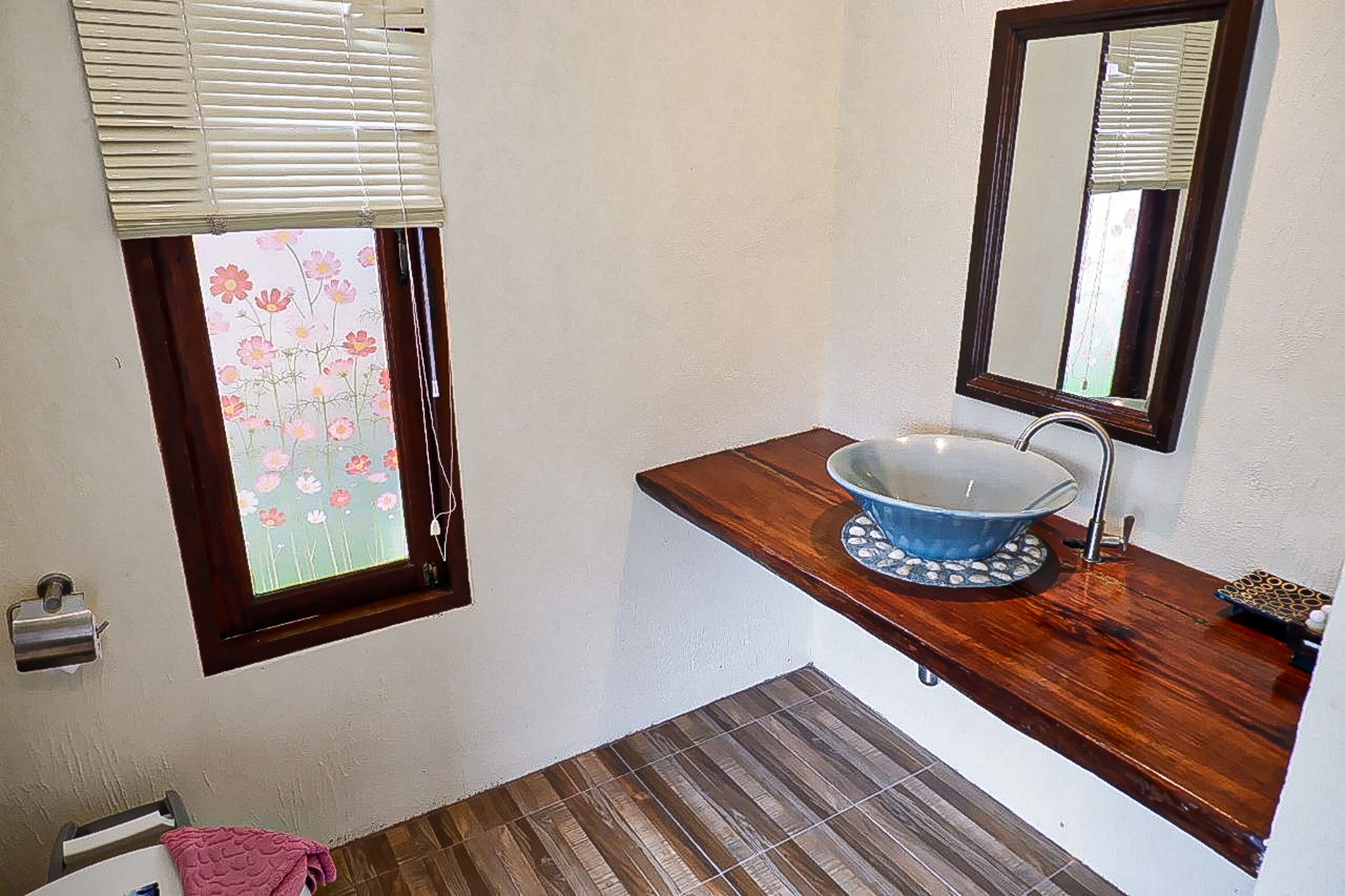 Une salle de bain avec un meuble-lavabo en bois, un lavabo bleu, un miroir et une fenêtre avec des stores.