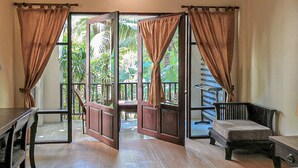 A room with a wooden floor, a bed, a bench, and a table. There are curtains on the windows, and a view of a balcony with plants. - Seashell Resort Koh Tao (Koh Tao)