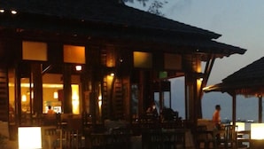 An outdoor seating area with tables and chairs, a covered section with a roof, and a view of the sea. - Seashell Resort Koh Tao (Koh Tao)