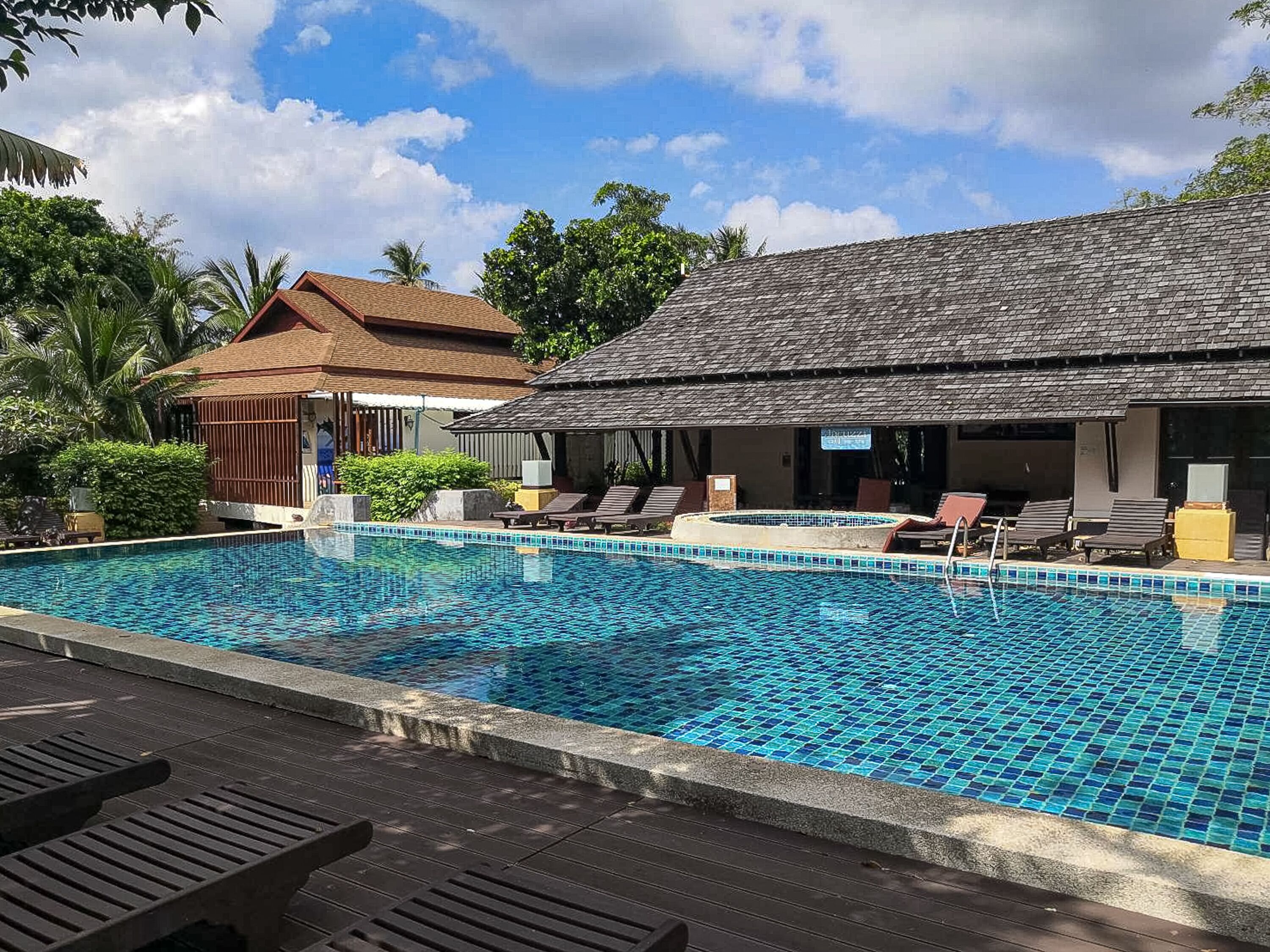 A swimming pool with lounge chairs and a covered area, surrounded by tropical vegetation and a clear sky.