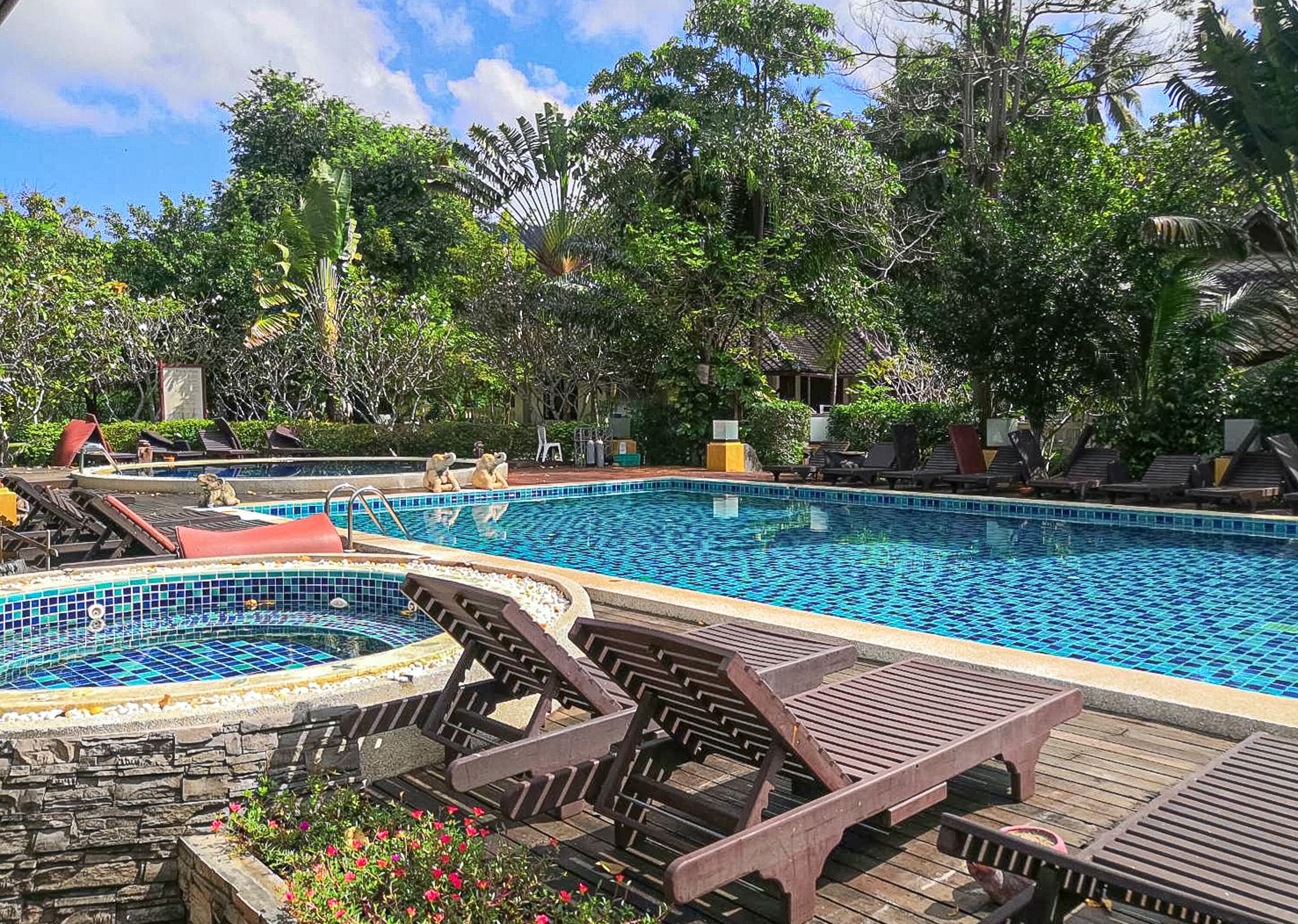 A swimming pool with lounge chairs and a hot tub, surrounded by lush greenery.