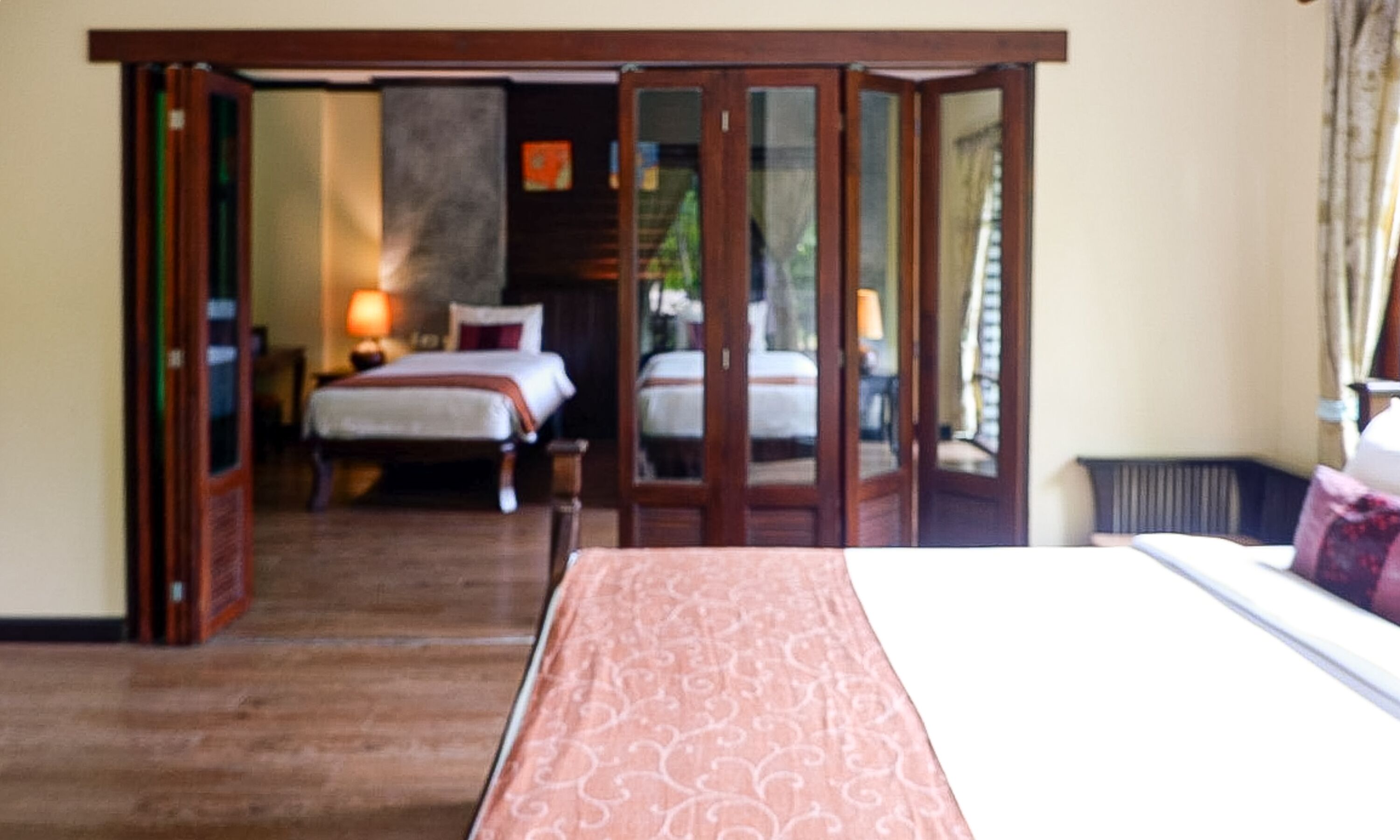 Une chambre d’hôtel dotée d’un grand lit, d’un coin salon séparé avec un fauteuil et une table, et offrant une vue à travers une porte vitrée.