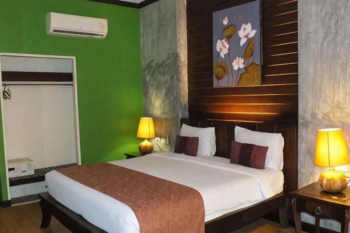 A hotel room with a bed, bedside lamps, a painting on the wall, and a wardrobe.